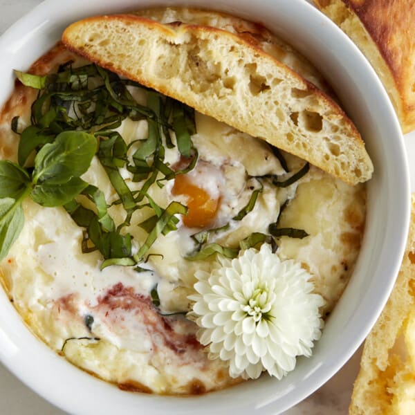 Overhead image of a ramekin with Eggs in Purgatory and a piece of bread on top.