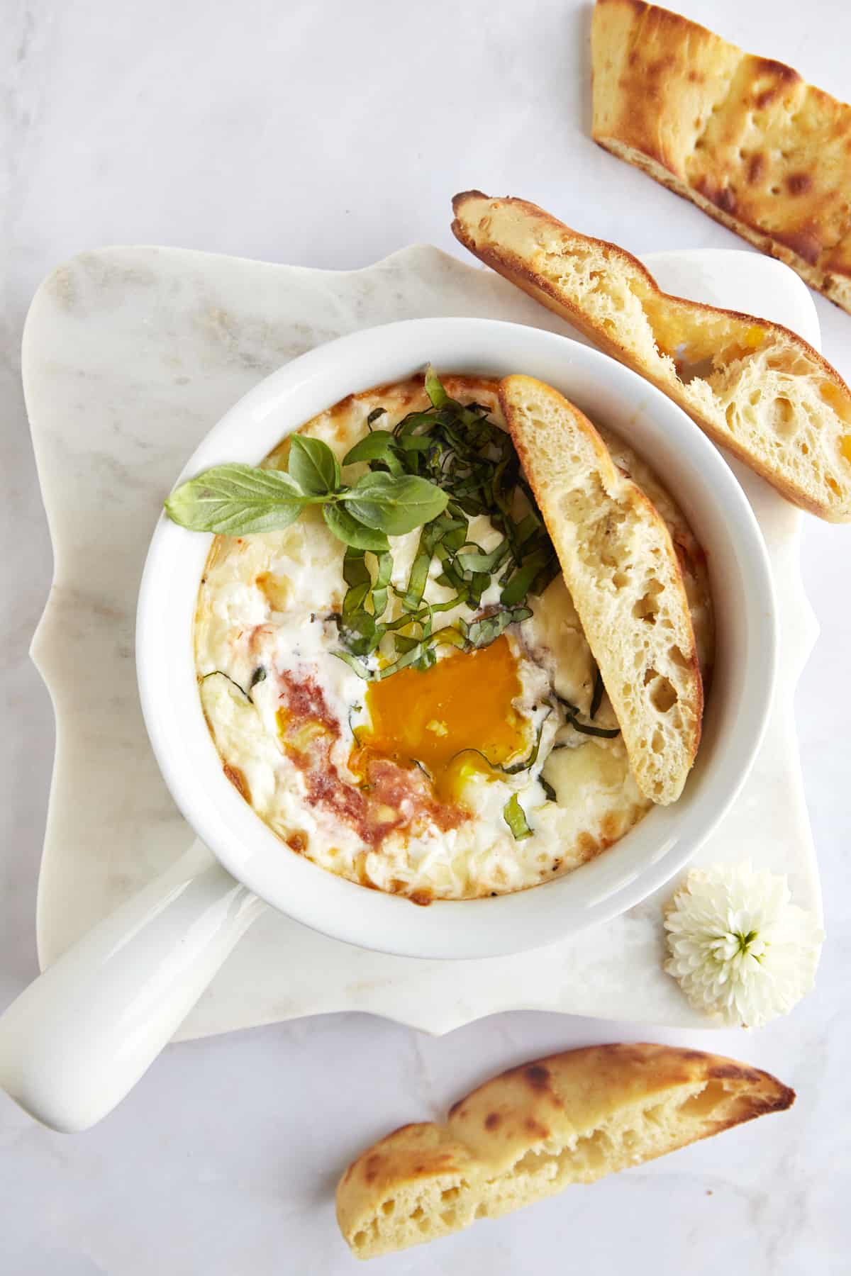 An egg yolk running over a ramekin full of Eggs in Purgatory with bread on the side. 