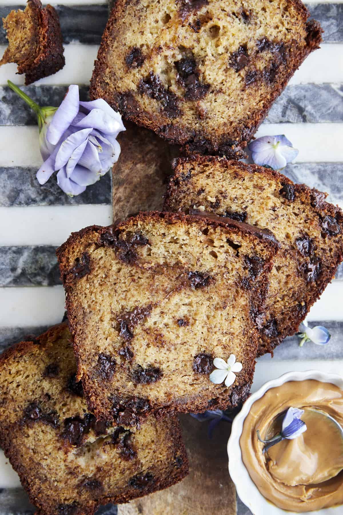 Slices of baked chocolate chip peanut butter banana bread with a small bowl of peanut butter on the side. 