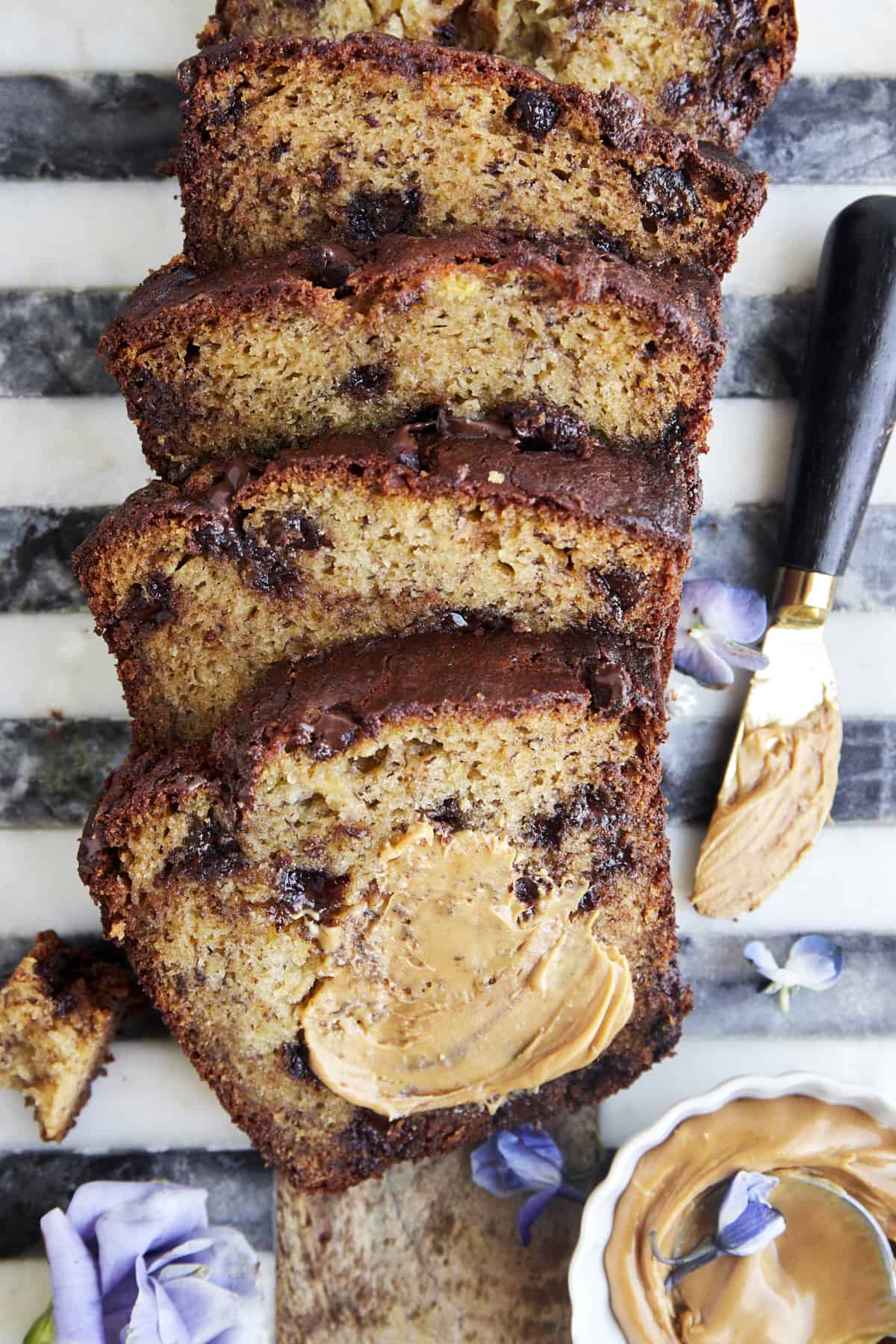 A sliced loaf of chocolate chip peanut butter banana bread with peanut butter smeared on the first slice. 