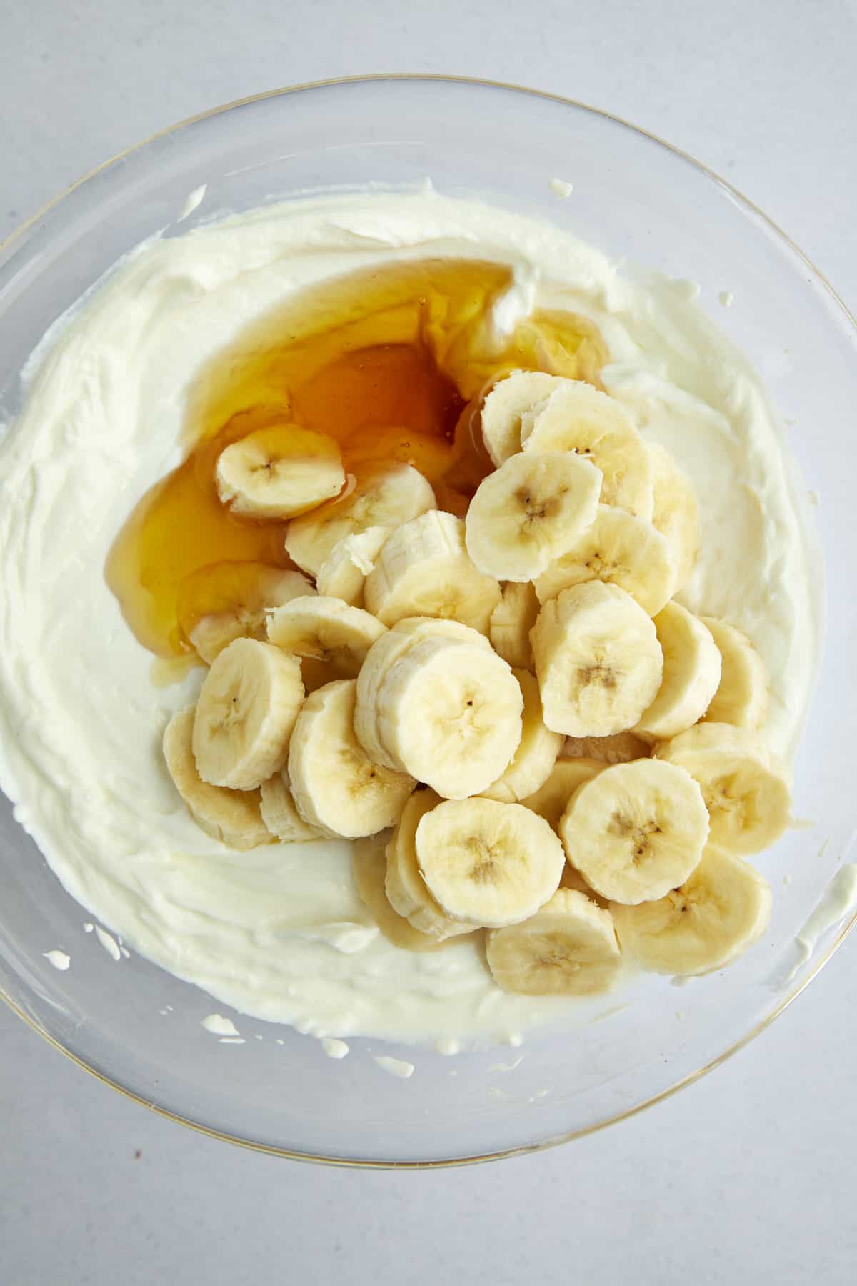 Overhead image of plain Greek yogurt, honey, and banana coins in a large mixing bowl. 