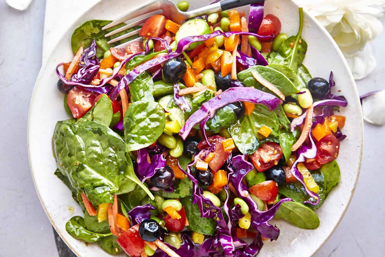 Overhead image of a bowl full of rainbow salad tossed with an olive oil dressing with a fork on the side. 