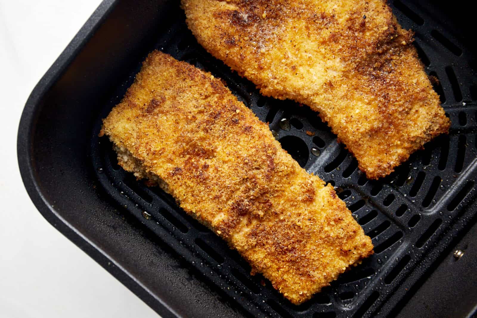 Two cooked Parmesan salmon filets in an air fryer basket. 