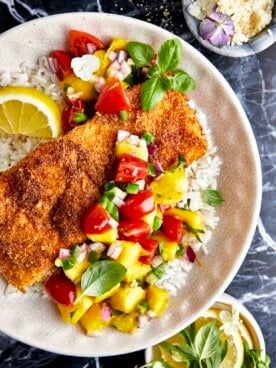 Parmesan crusted salmon with mango salsa on a plate with rice.