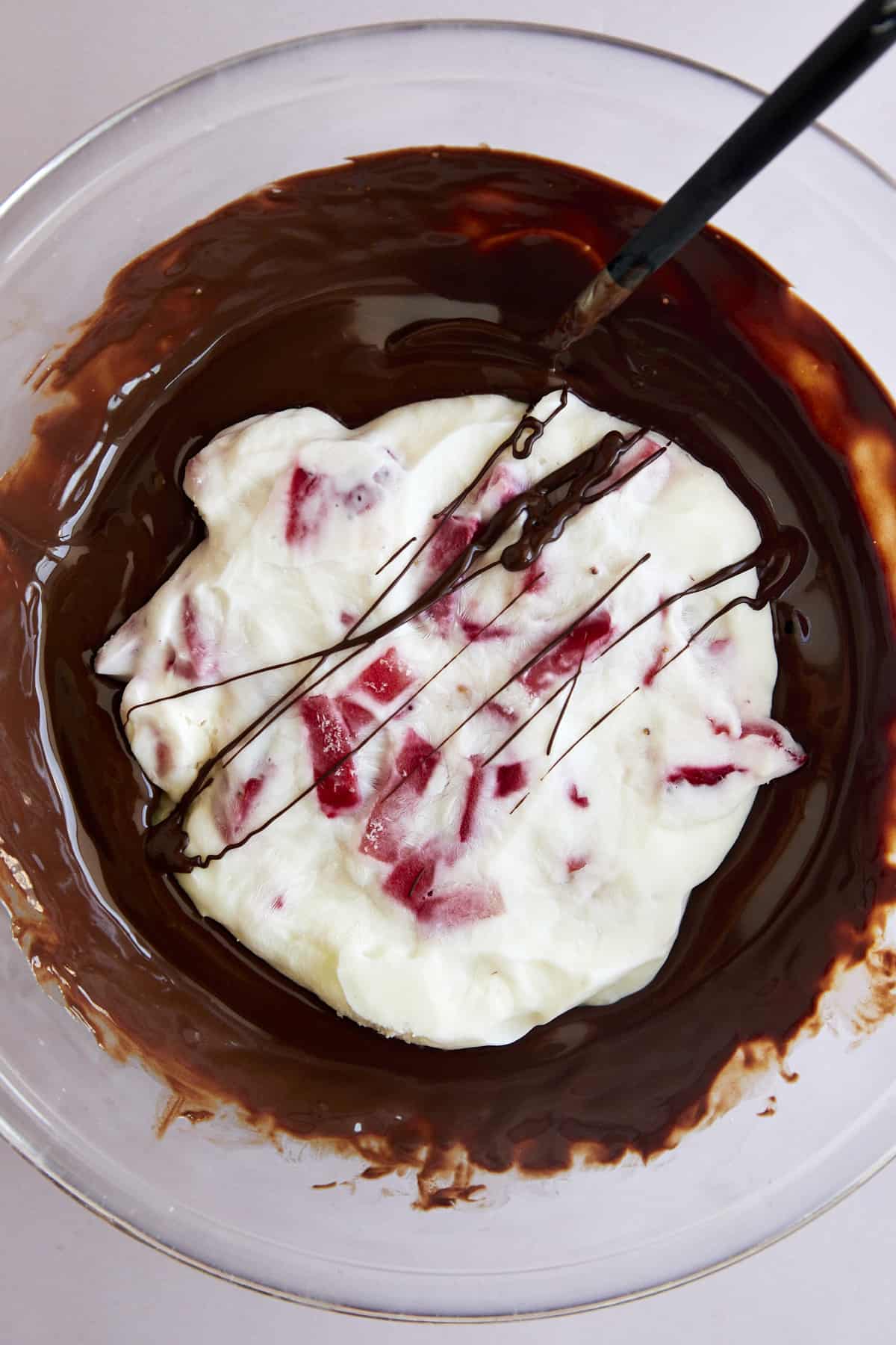 Overhead image of a strawberry yogurt cluster in a bowl of melted chocolate. 