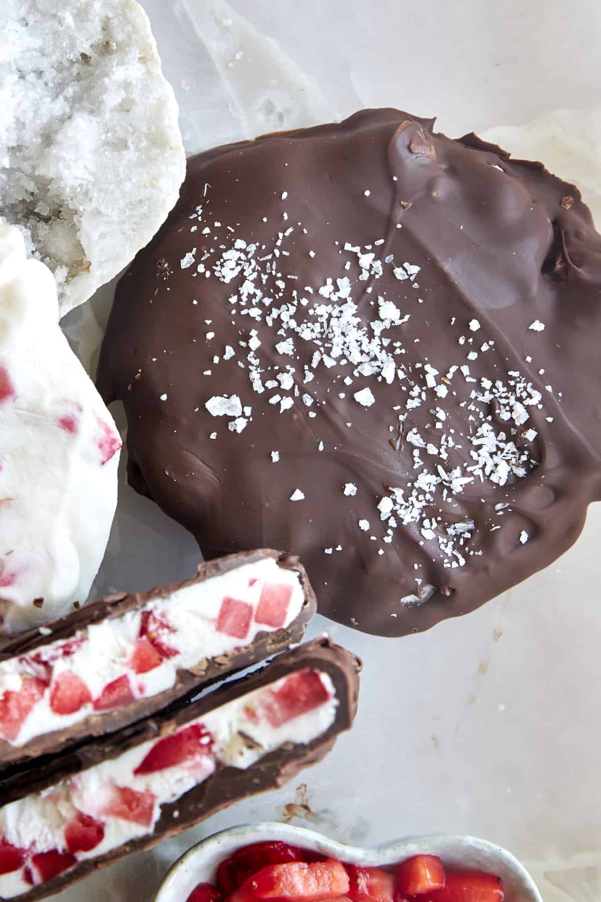 Two chocolate strawberry yogurt clusters topped with salt with one split in half. 
