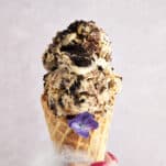 A hand holding a waffle cone stuffed with two scoops of mocha Oreo no churn ice cream.