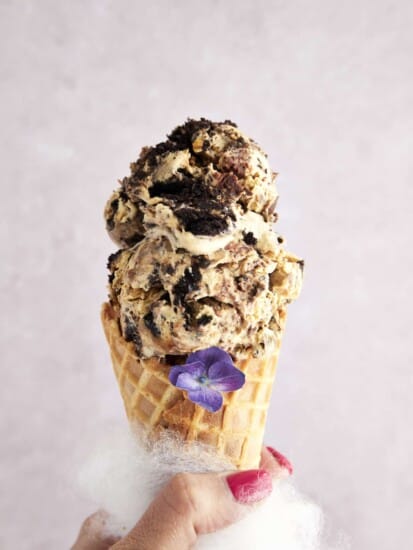 A hand holding a waffle cone stuffed with two scoops of mocha Oreo no churn ice cream.