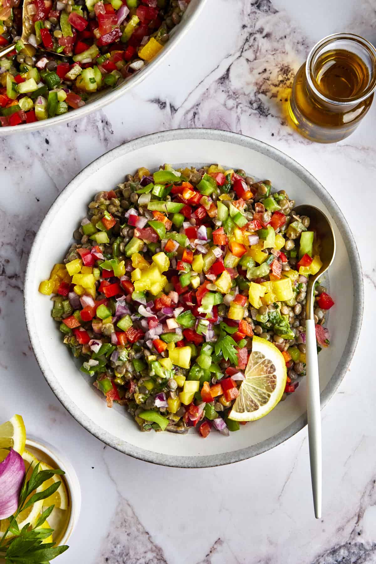 Overhead image of a bowl of lentil mango salad with a spoon on the side and a lemon wedge on top. 