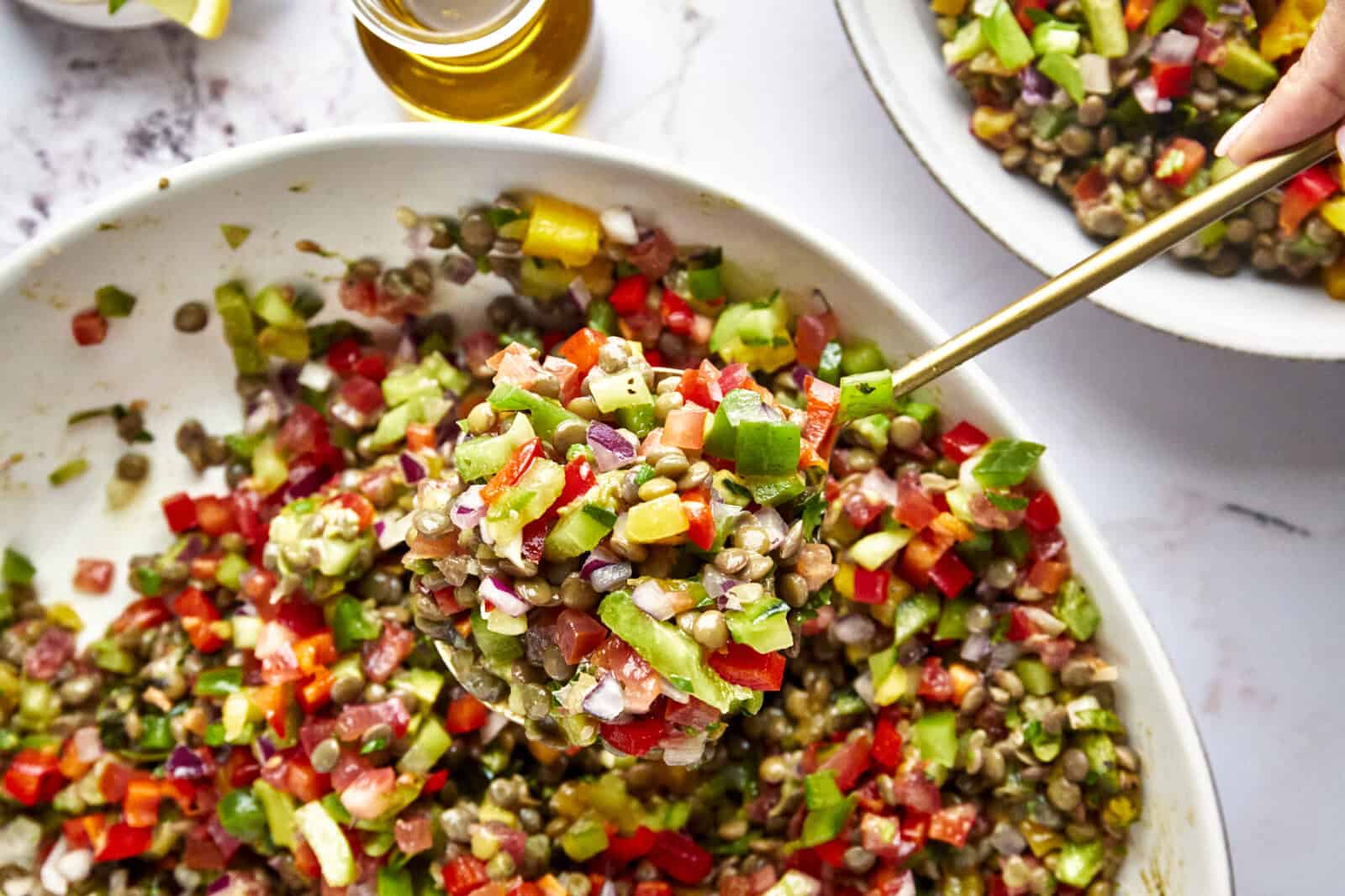 A serving spoon lifting a scoop of lentil mango salad from a bowl. 