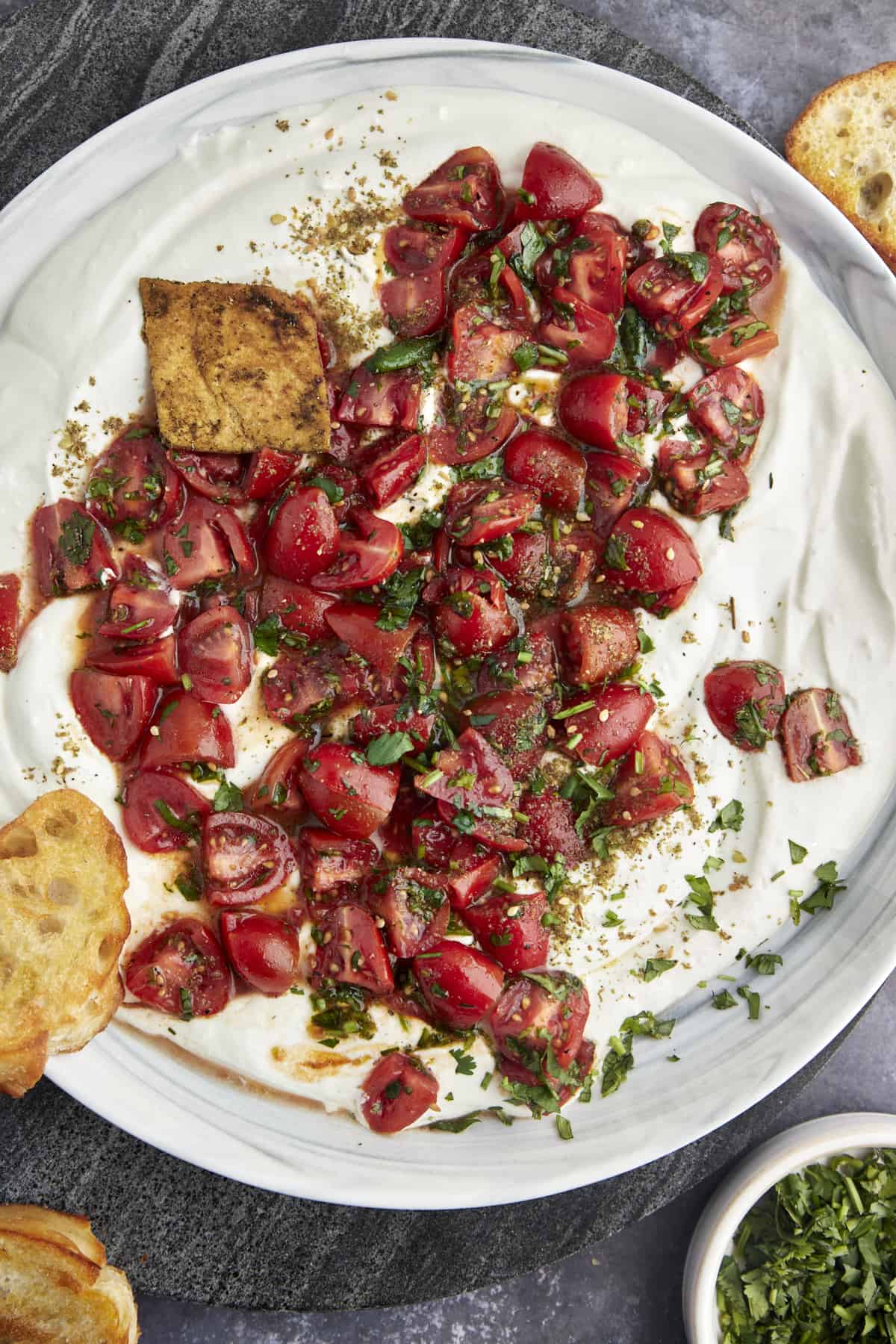 Overhead image of a savory whipped cottage cheese and tomatoes bowl with crostini and pita chips on the side. 