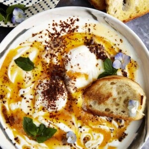 A bowl of Turkish poached eggs with cottage cheese with a piece of bread.