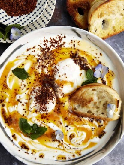 A bowl of Turkish poached eggs with cottage cheese with a piece of bread.