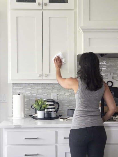 A woman using a microfiber cloth to wipe down kitchen cabinets.