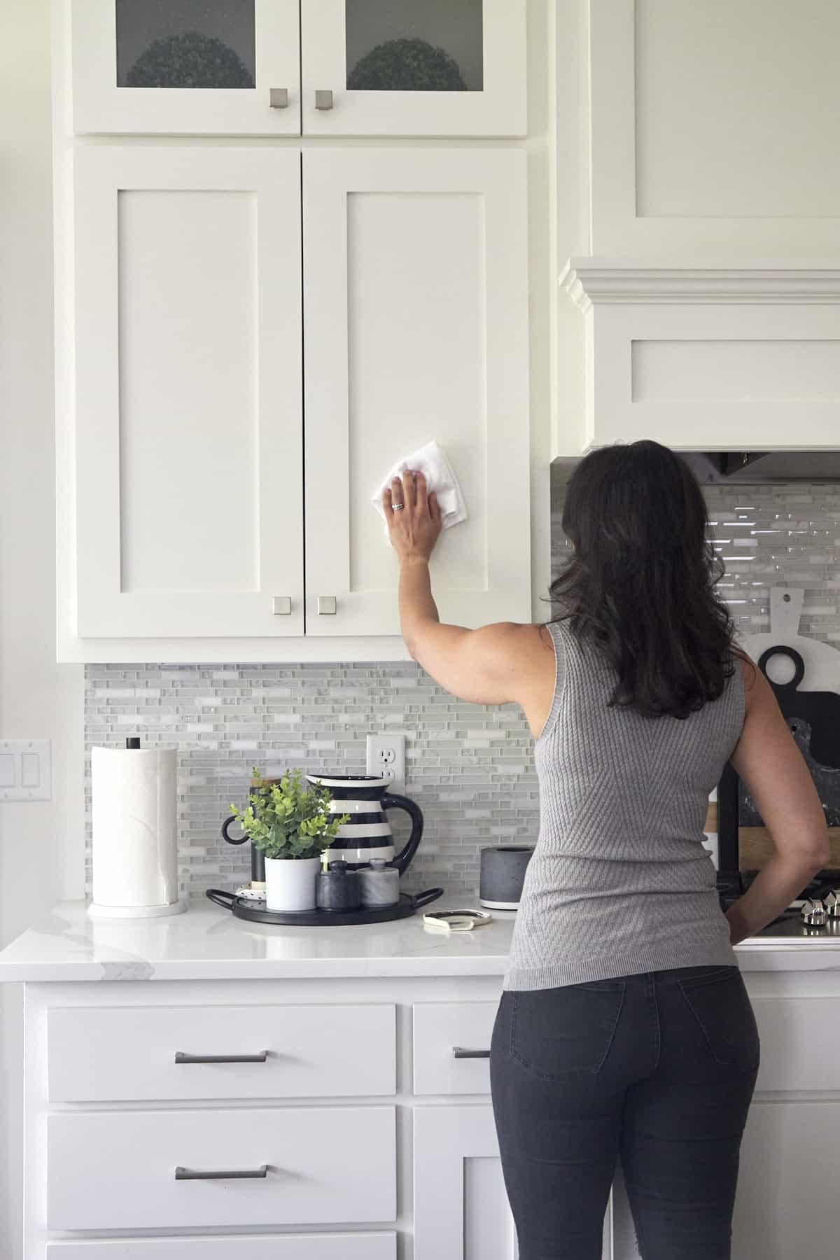 A woman using a microfiber cloth to wipe down kitchen cabinets. 