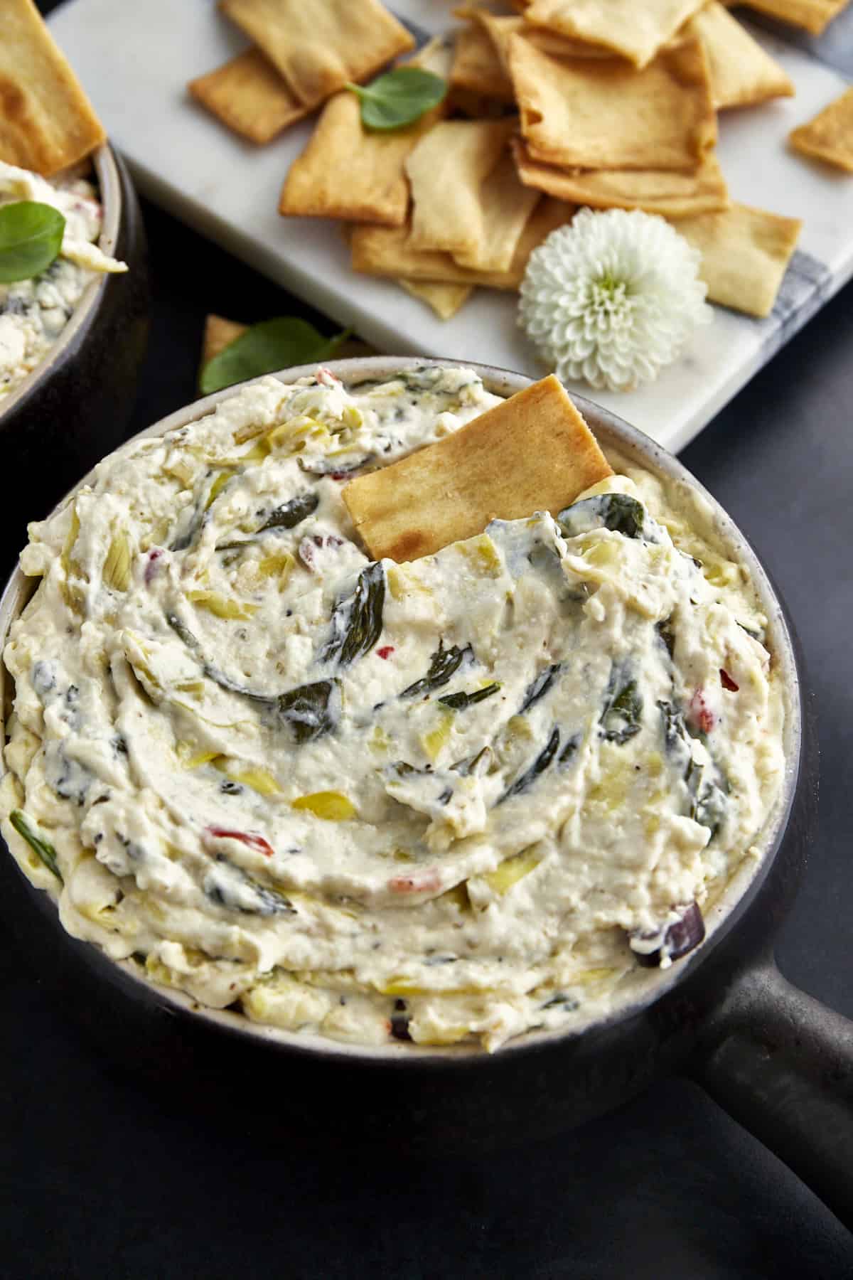 A bowl of spinach and artichoke dip with a cracker sticking out. 