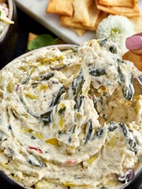 A chip scooping up spinach and artichoke dip from a bowl.