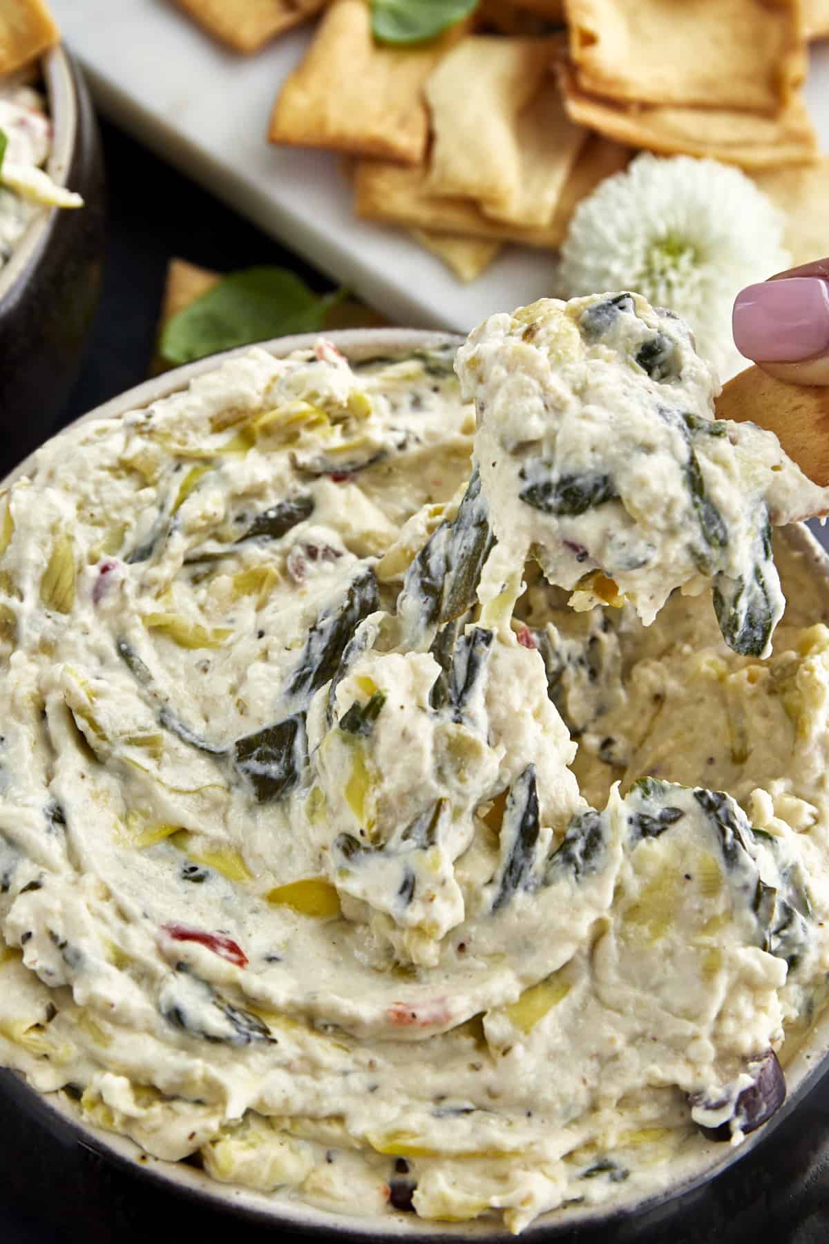 A chip scooping up spinach and artichoke dip from a bowl.