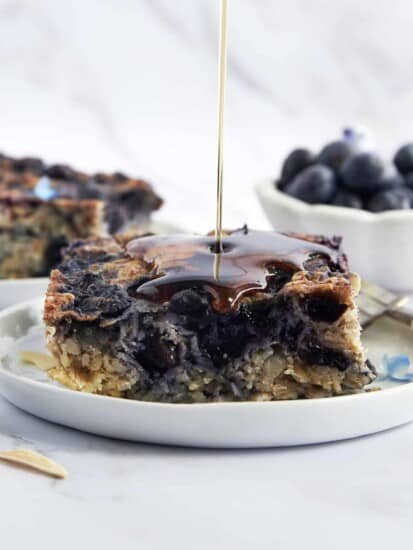 A plate with a serving of blueberry baked oatmeal with maple syrup being drizzled on top.