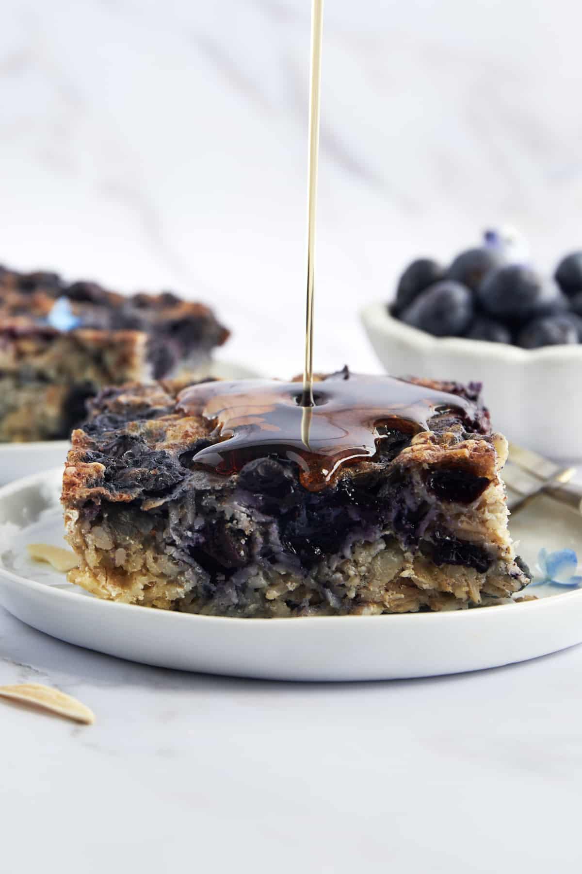 A serving of blueberry baked oatmeal with maple syrup being poured on top. 