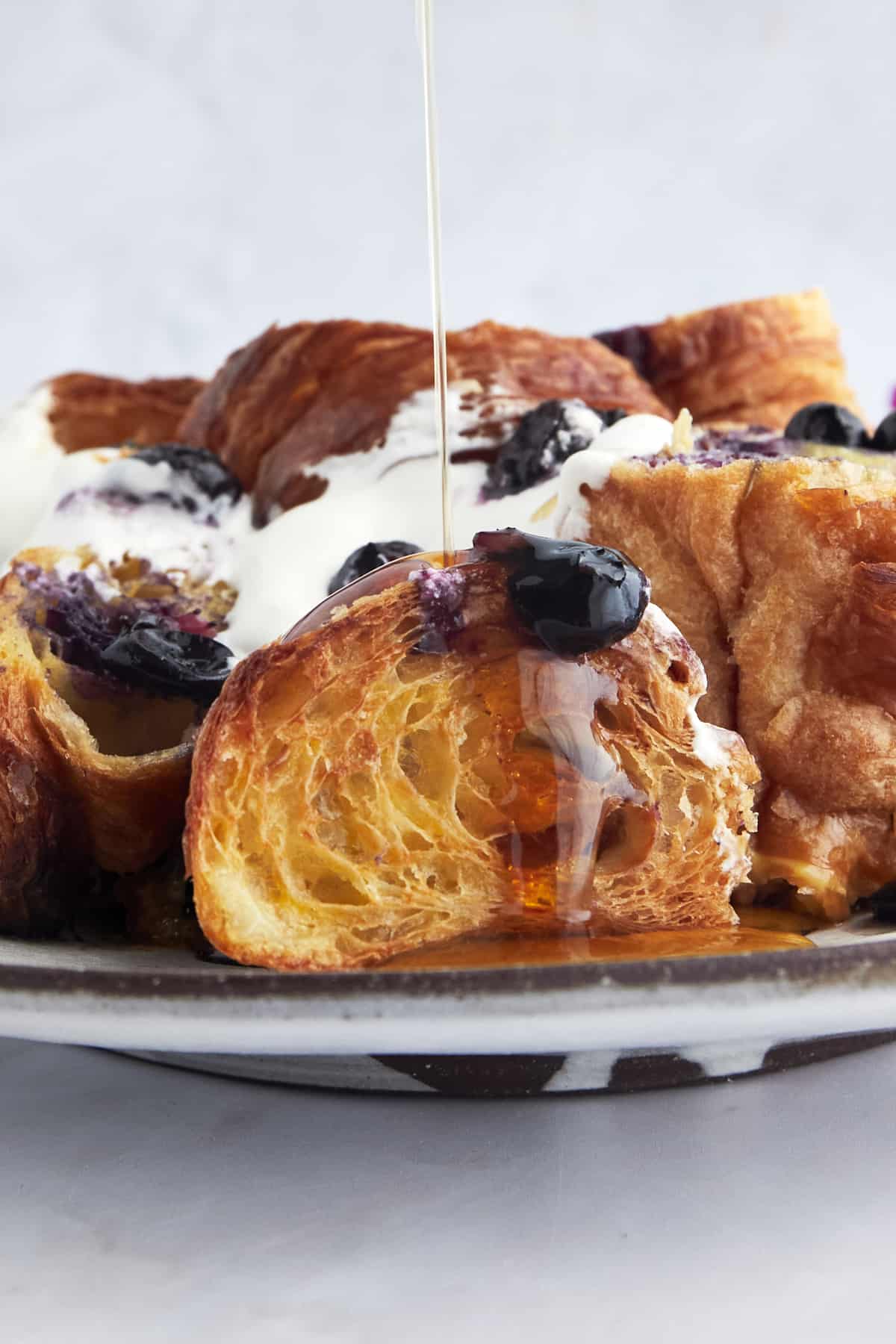 Close up image of maple syrup being drizzled over blueberry French toast. 