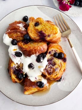 A plate full of croissant blueberry French toast topped with yogurt, blueberries, and maple syrup.