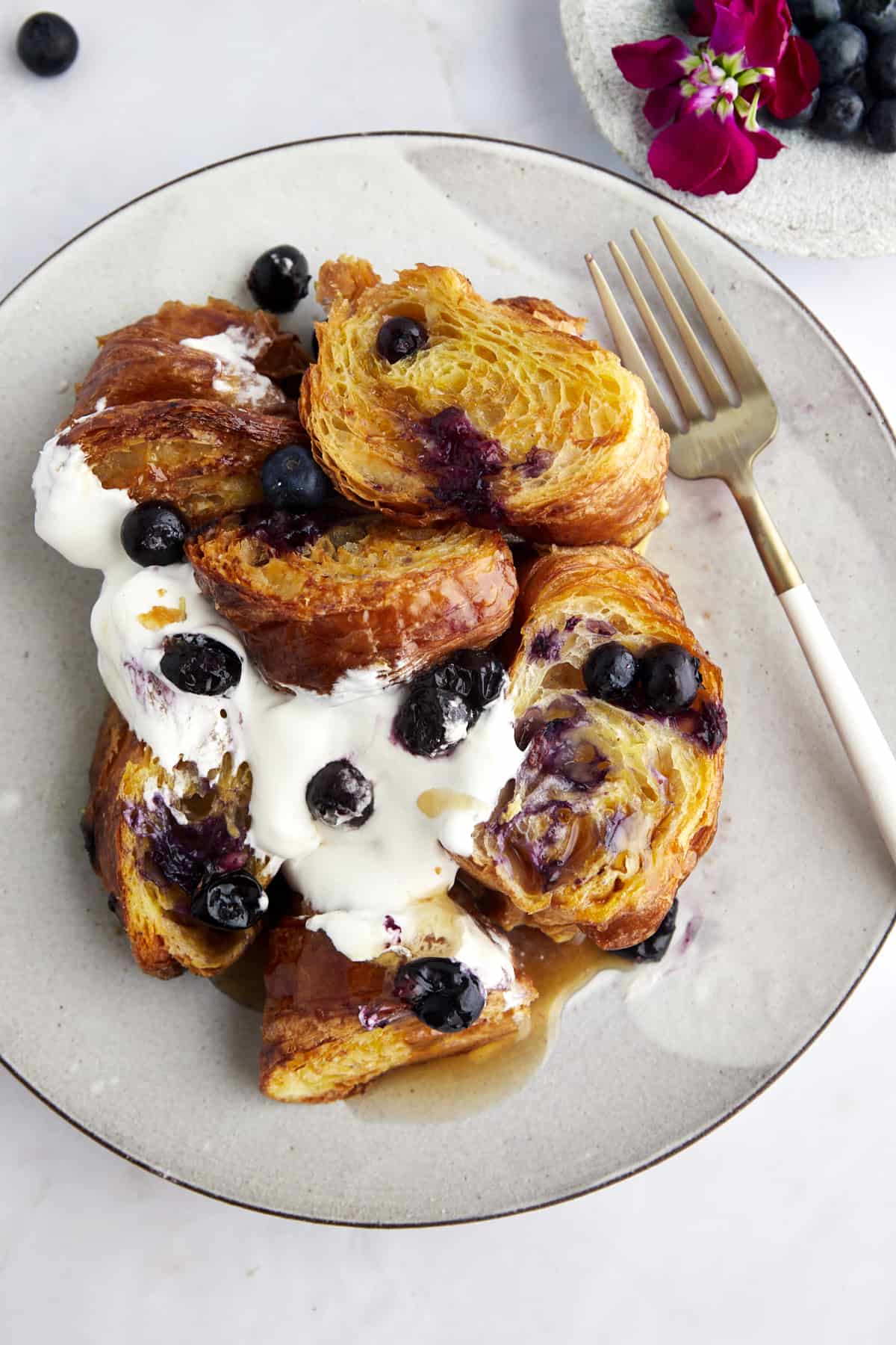 A plate of croissant blueberry French toast topped with yogurt, blueberries,  and syrup. 
