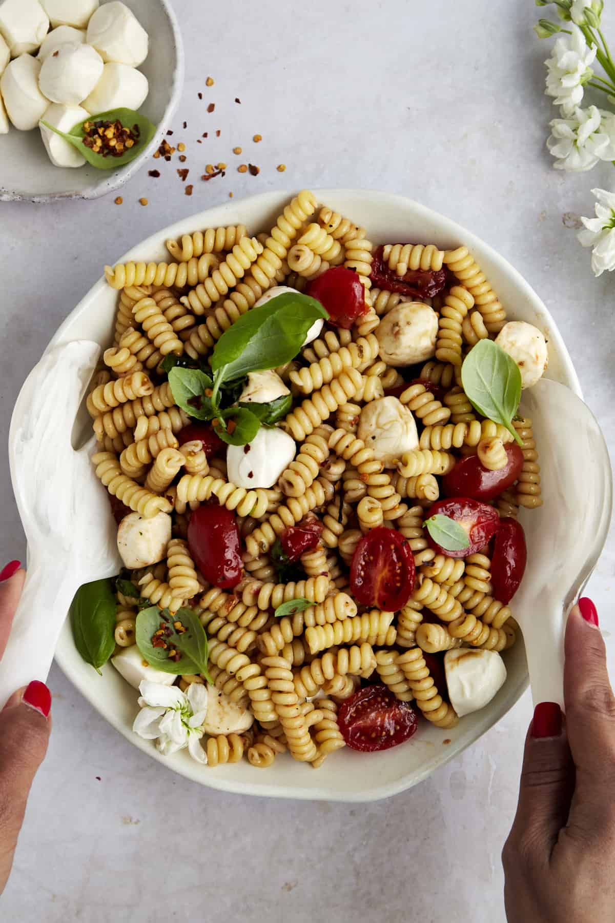 Two hands tossing caprese pasta salad in a bowl.
