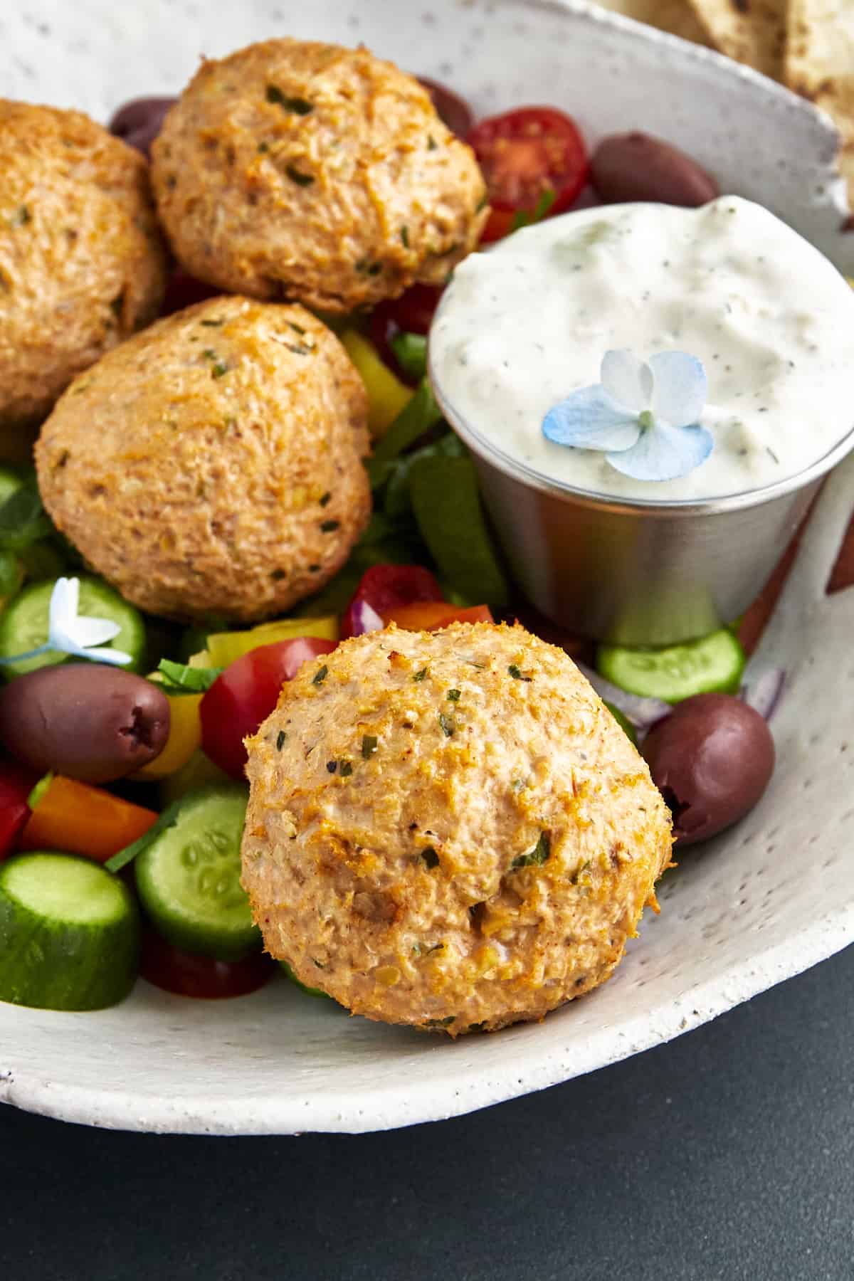 Close up image of baked chicken shawarma meatballs with a side of tzatziki. 