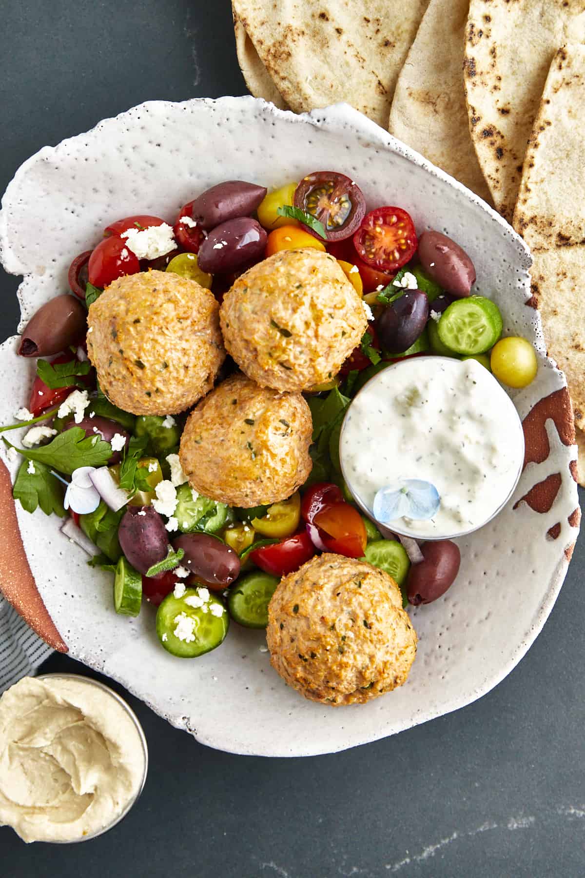 Overhead image of a bowl of baked chicken shawarma meatballs, veggies, and tzatziki.