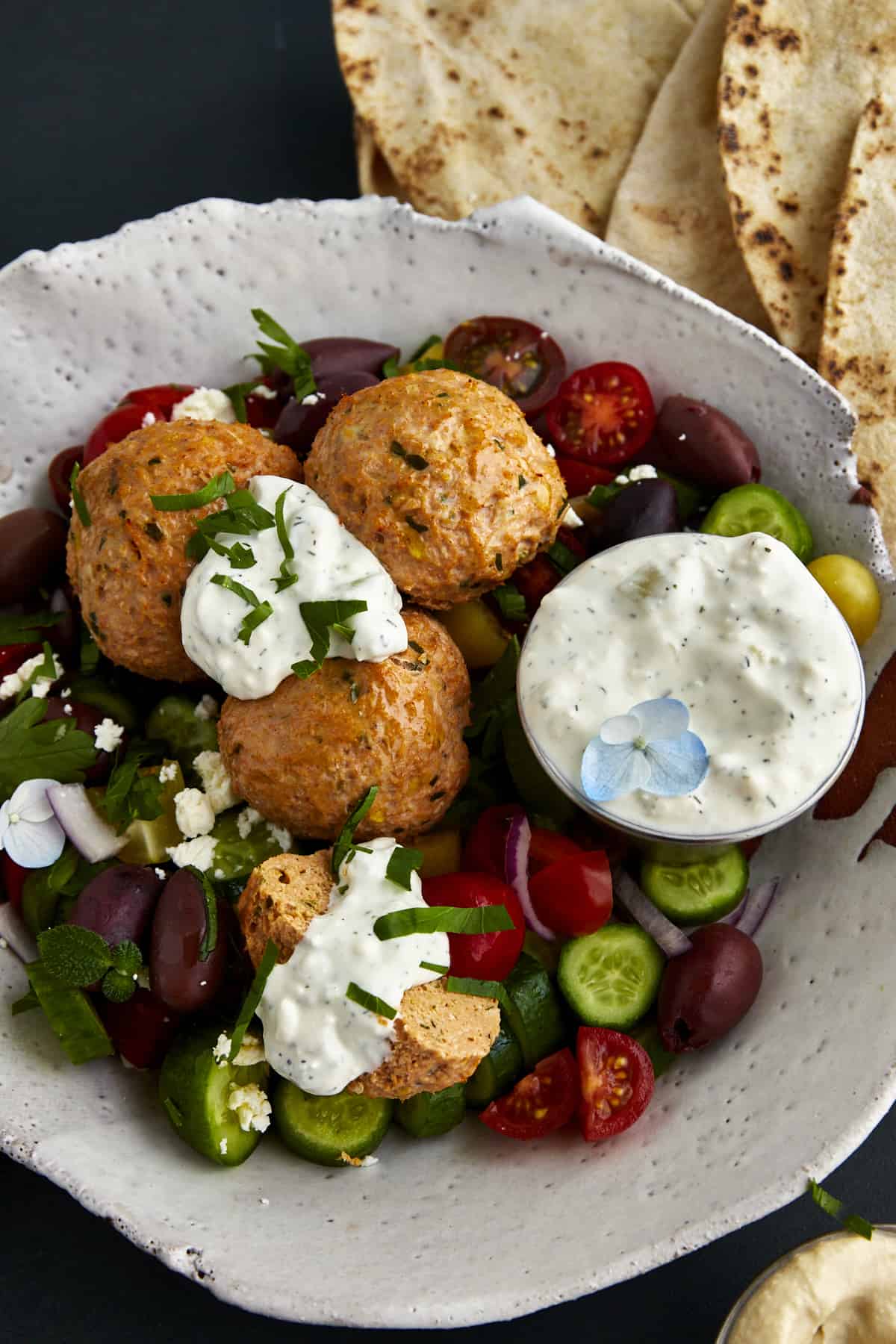 A bowl of chicken shawarma meatballs with cucumbers, tomatoes, olives, and tzatziki. 