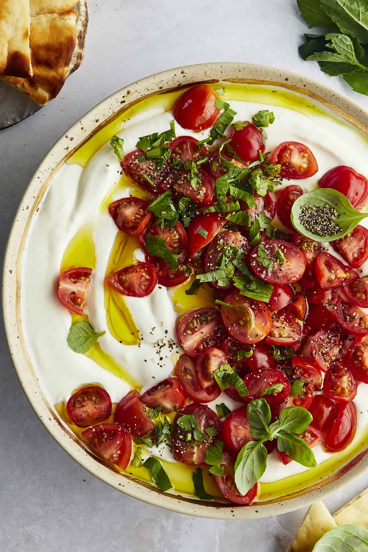 A bowl of marinated tomatoes and whipped feta dip topped with herbs and olive oil. 