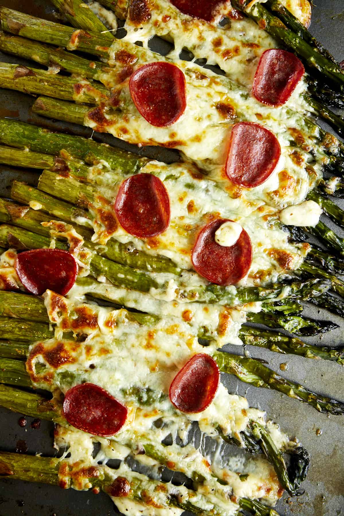 Overhead image of oven roasted asparagus topped with cheese and pepperoni. 
