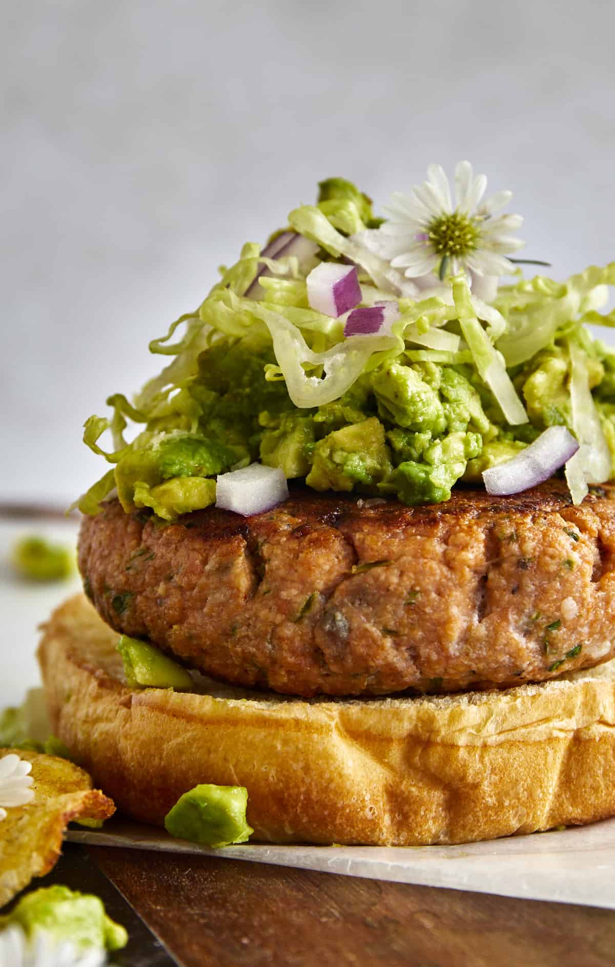 Close up image of an open-faced salmon burger with avocado, red onion, and shredded lettuce. 