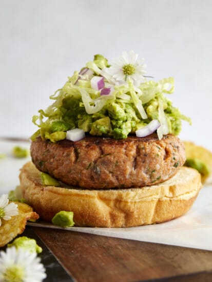 An open-faced salmon burger with avocado, lettuce, and red onion.