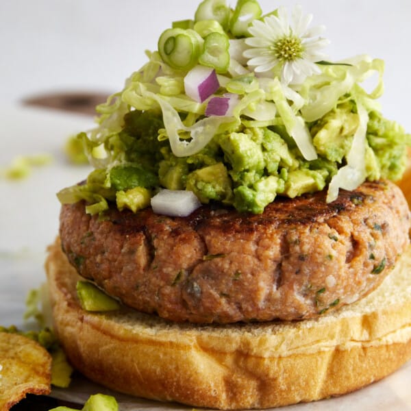 A salmon burger topped with avocado, red onion, shredded lettuce, and green onion.