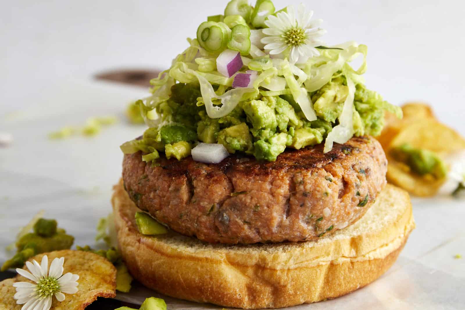 A salmon burger topped with avocado, red onion, shredded lettuce, and green onion.