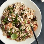 A bowl of shrimp orzo bake topped with fresh herbs with a spoon sticking out.