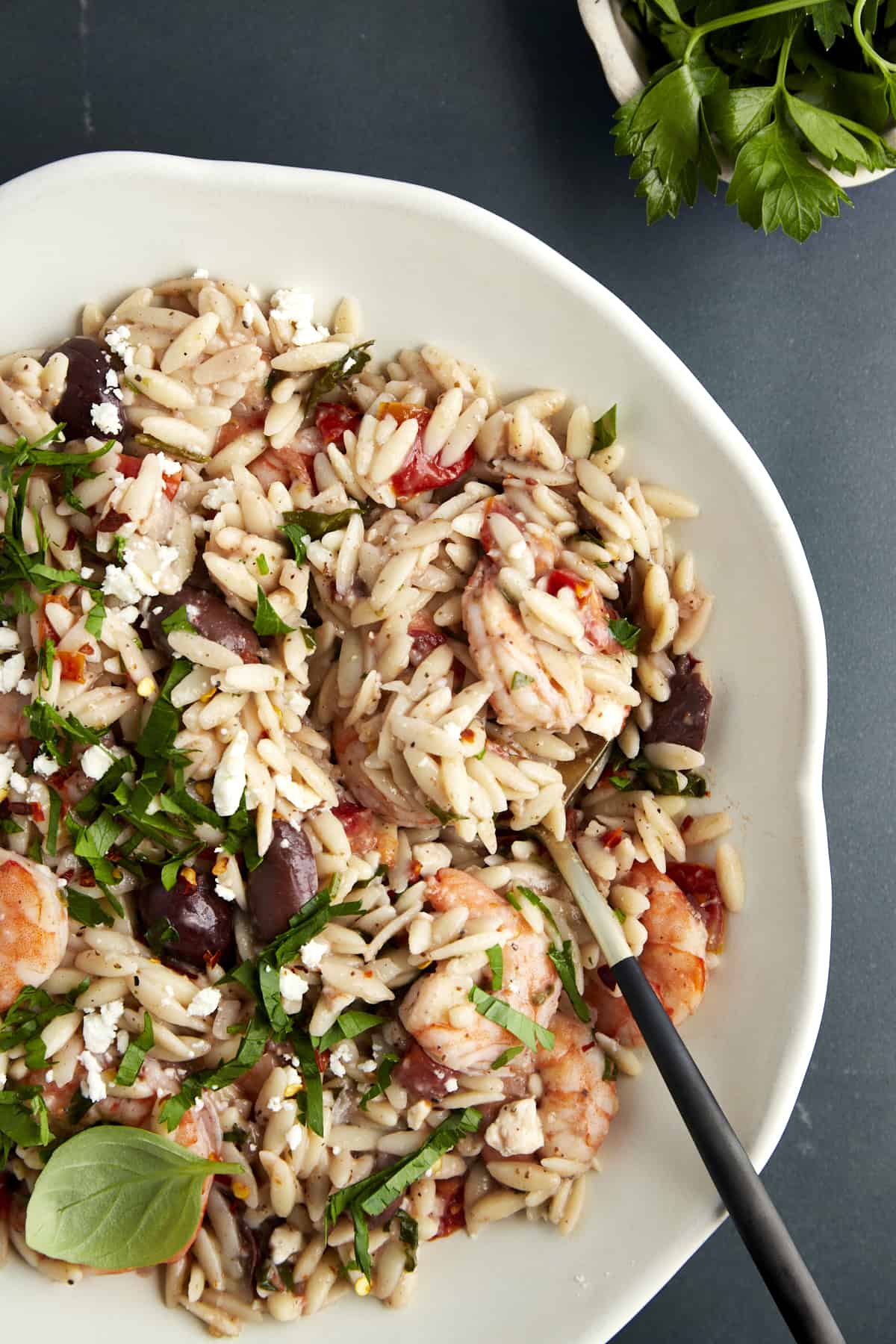 A bowl of shrimp orzo bake topped with fresh herbs and feta. 