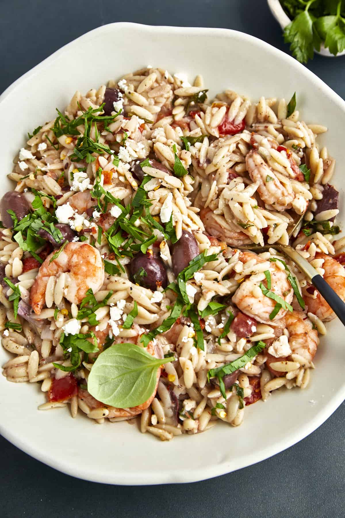 A bowl of shrimp and orzo with tomatoes, red onions, olives, fresh herbs, and feta. 