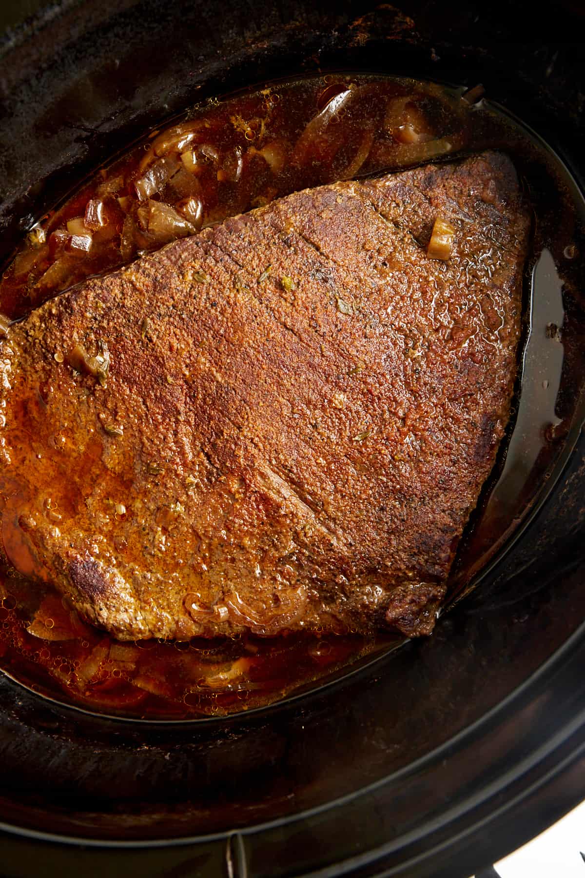 A cooked beef brisket in a slow cooker with onions. 