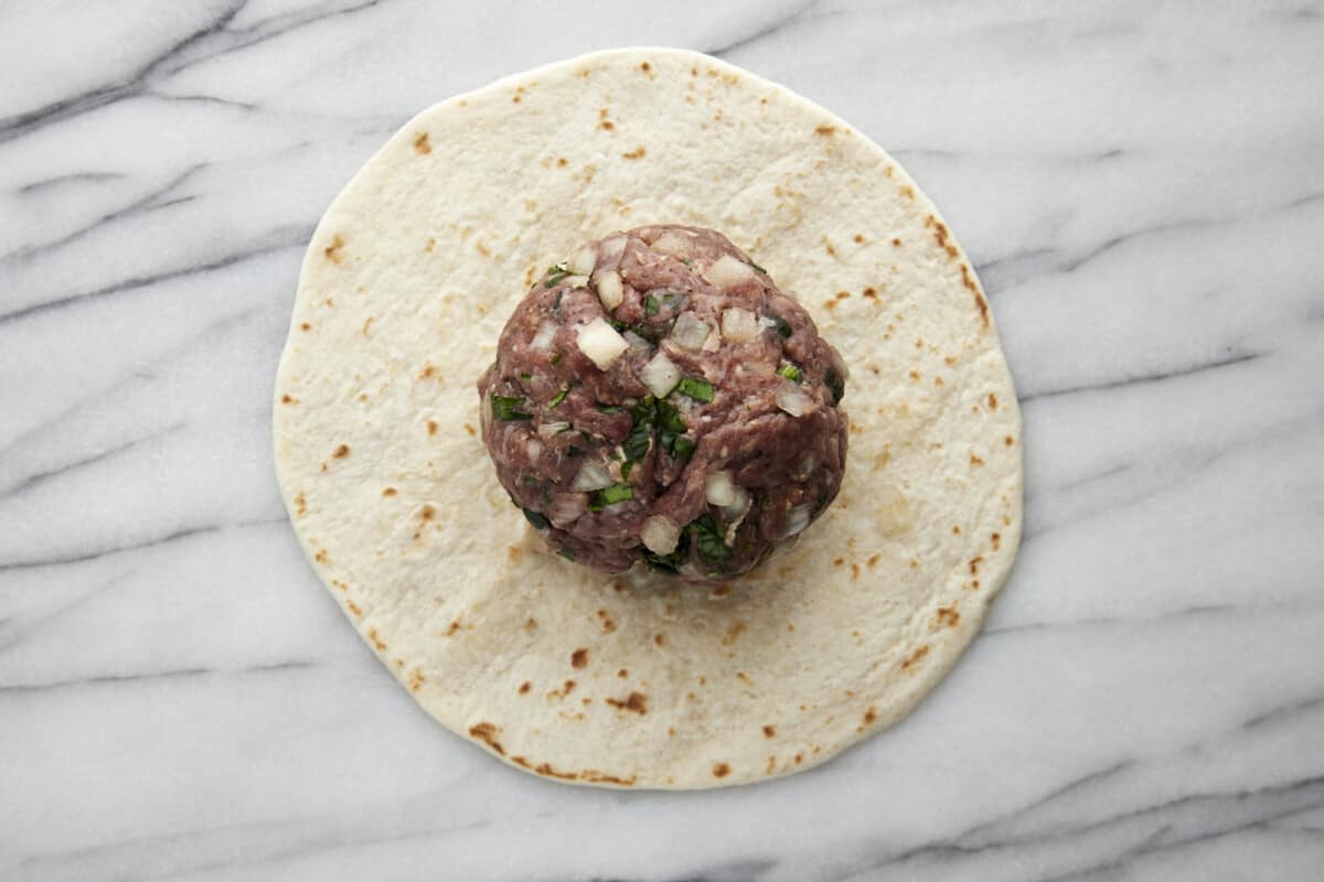 Seasoned ground beef patty on top of a tortilla. 