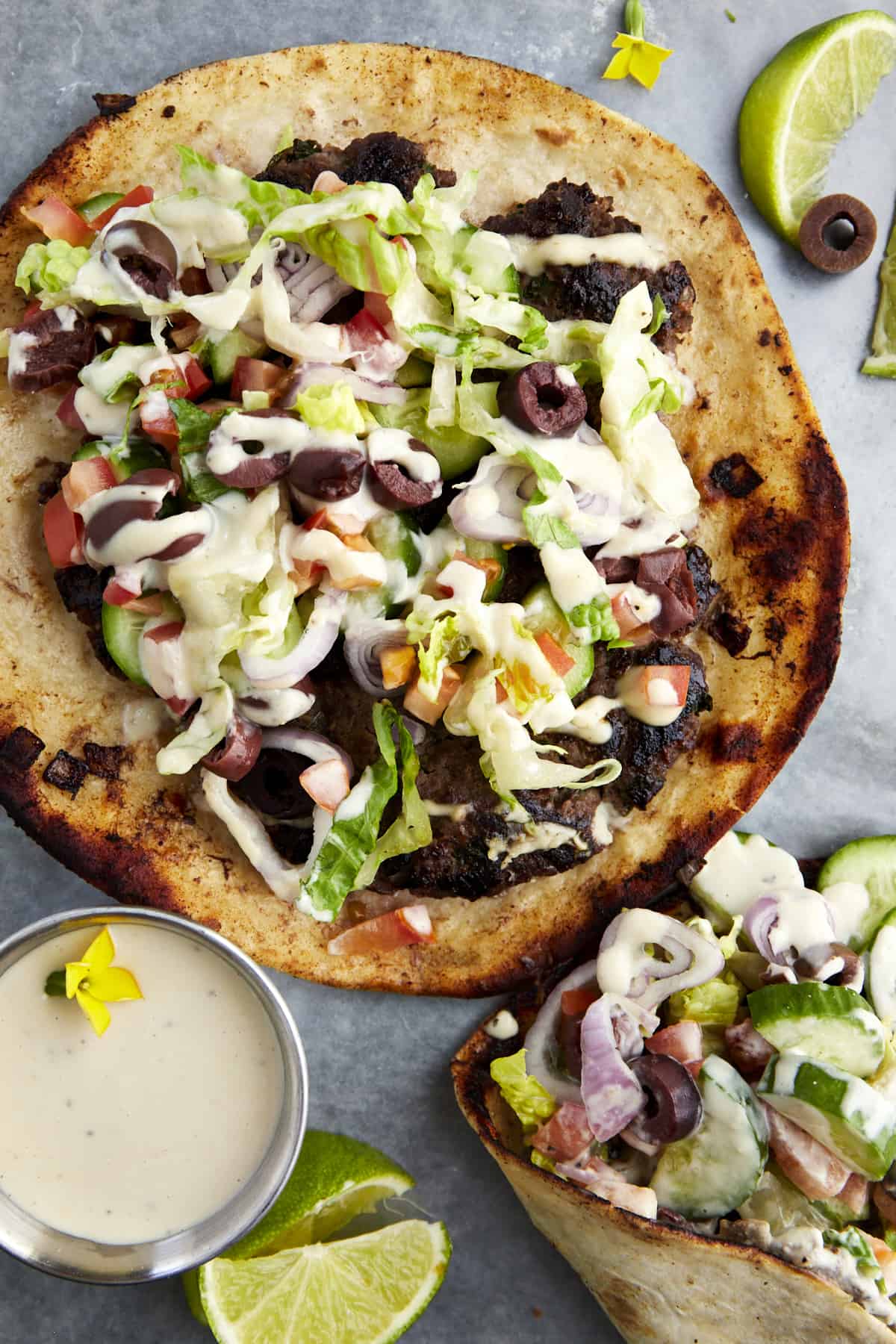 Greek-inspired smashed taco topped with lettuce, onion, tomatoes, olives, and tahini. 