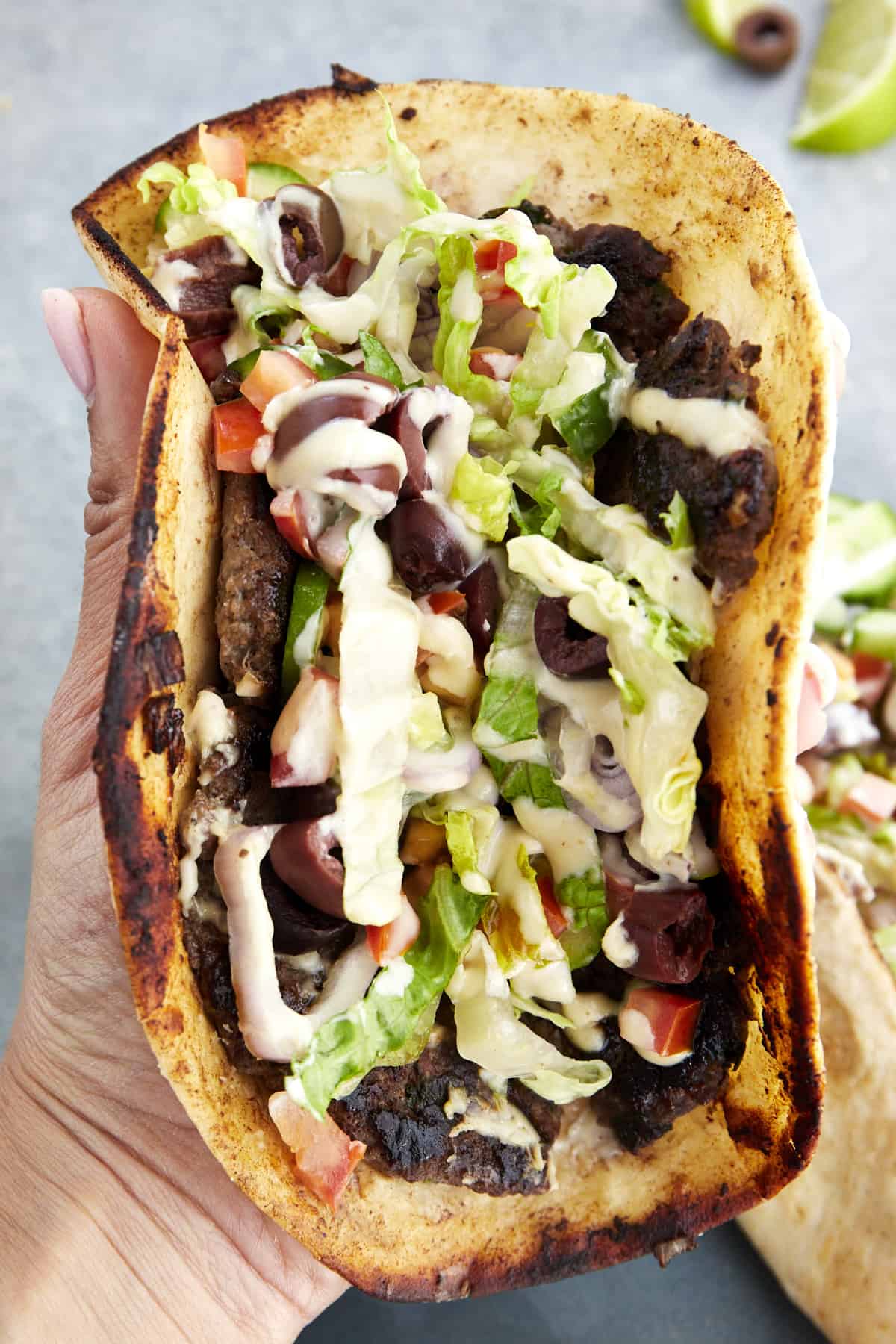 A hand holding a folded Greek-inspired smashed taco. 