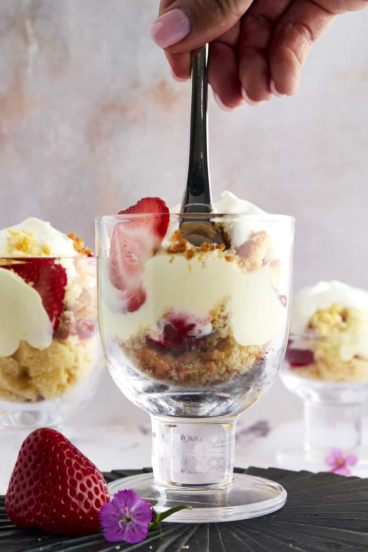 A hand holding a fork dipped into the center of a strawberry shortcake shooter. 