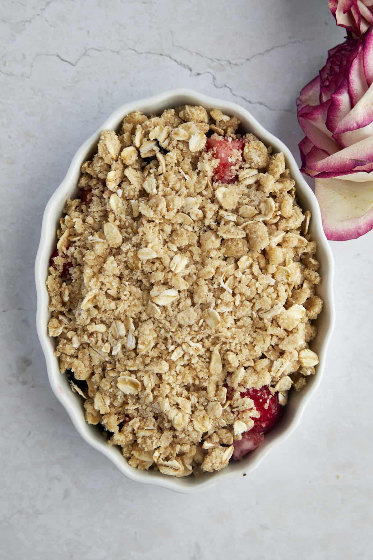 An unbaked mixed berry crisp in a white oval baking dish.
