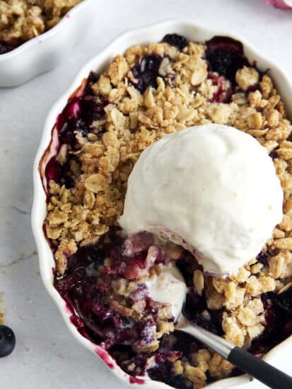 Overhead image of a mixed berry crisp topped with ice cream with a spoon taking a scoop.