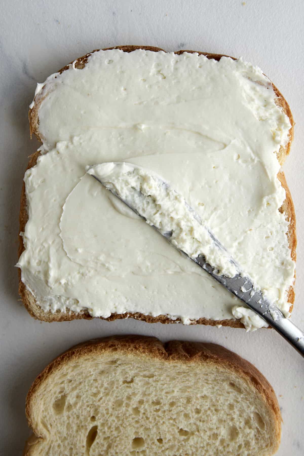 Cream cheese being spread over a piece of bread. 