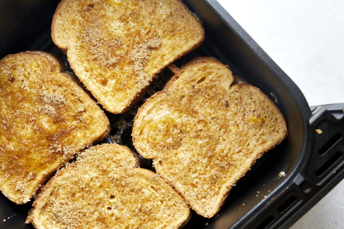 Four uncooked cream cheese stuffed french toast sandwiches in an air fryer basket. 