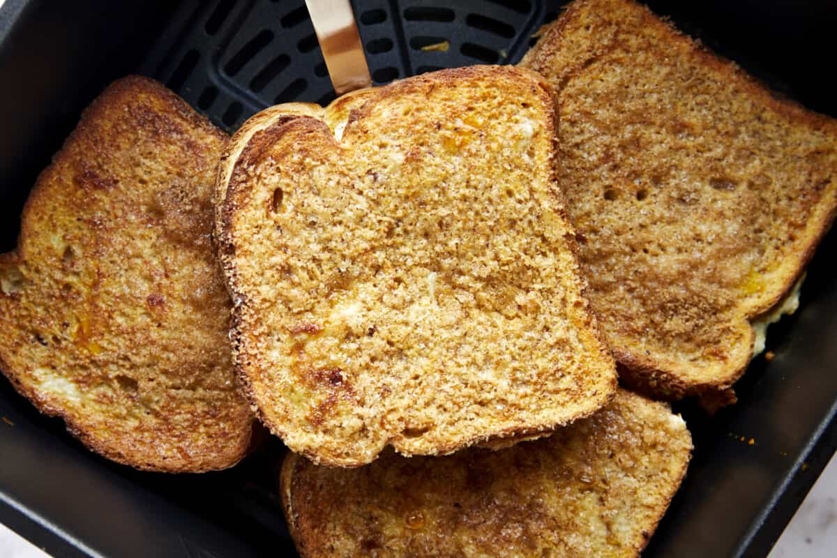 Four cooked cream cheese stuffed air fryer french toast sandwiches in an air fryer basket. 